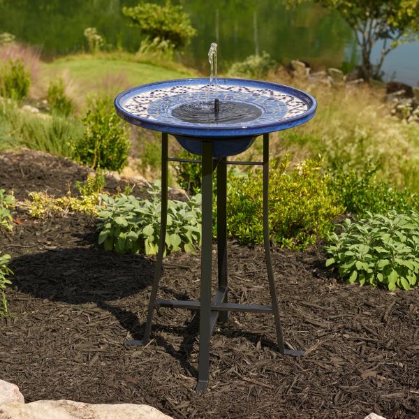 Blue ceramic bird bath with a stand in a garden setting