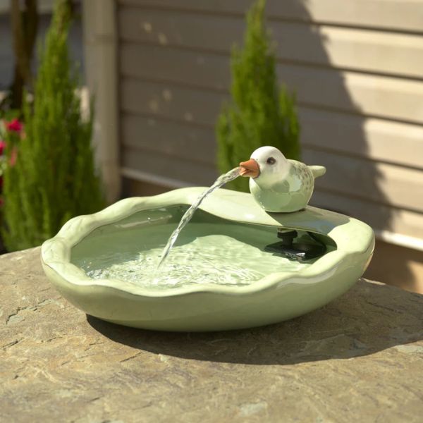 Decorative bird bath with a bird figurine pouring water into a bowl on a stone surface.