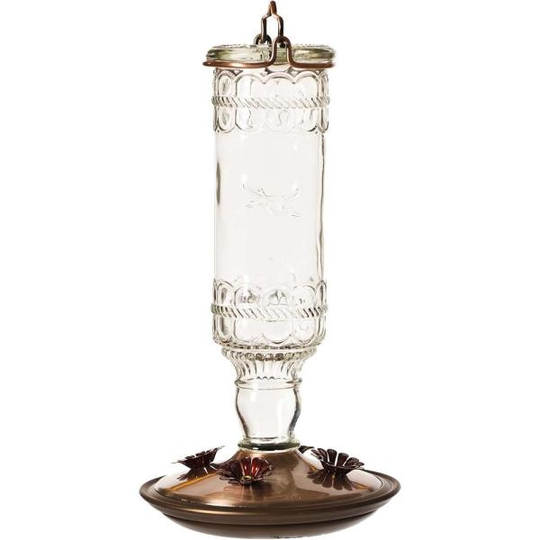 Clear glass hummingbird feeder with decorative base on a white background