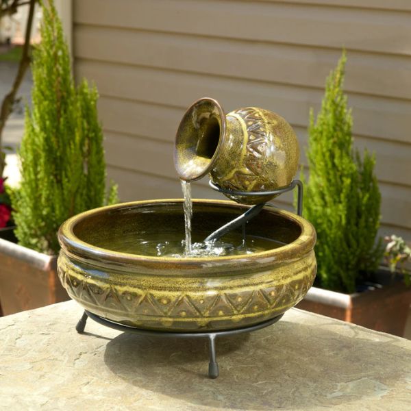 Decorative outdoor water fountain with greenish-brown ceramic design on a stone surface.