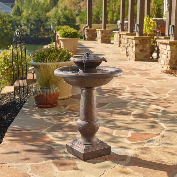Decorative outdoor fountain on a stone patio with a scenic background