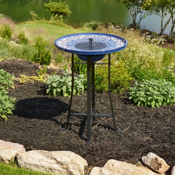 Blue ceramic bird bath in a garden setting with greenery and rocks.