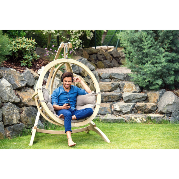 Man sitting in a circular wooden swing chair in a garden setting.