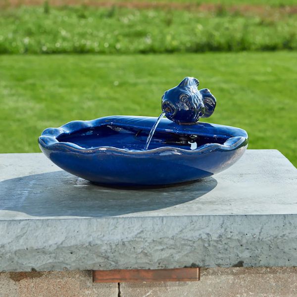 Blue ceramic bird bath with a flowing water feature on a stone ledge.