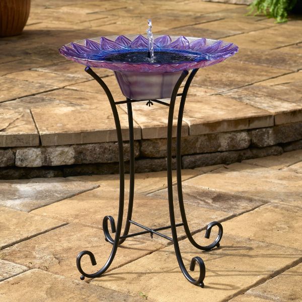 Decorative glass bird bath on a metal stand outdoors.