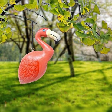 Pink flamingo ornament hanging from a tree branch with green leaves and grass in the background
