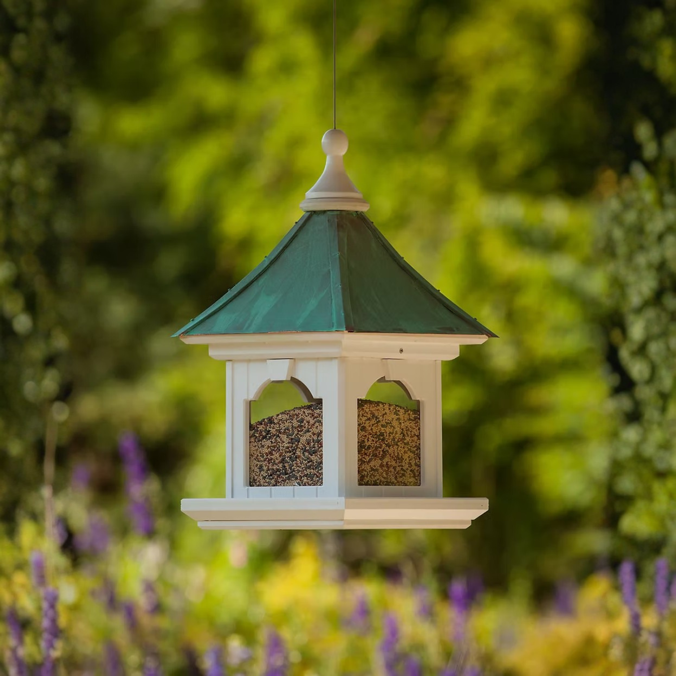 Bird feeder with Patina Copper roof and beige body hanging against a blurred garden background