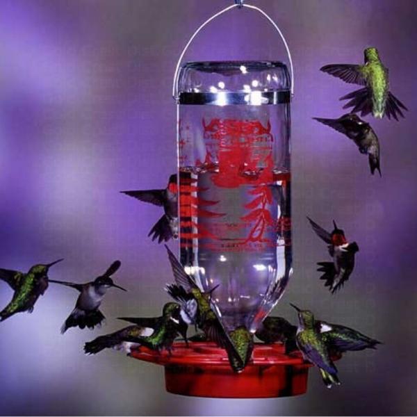 Hummingbird feeder with red nectar solution and hummingbirds around it on a purple background