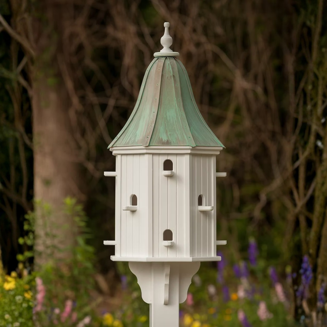 Decorative birdhouse with multiple perch entry points and a patina copper roof in a garden setting