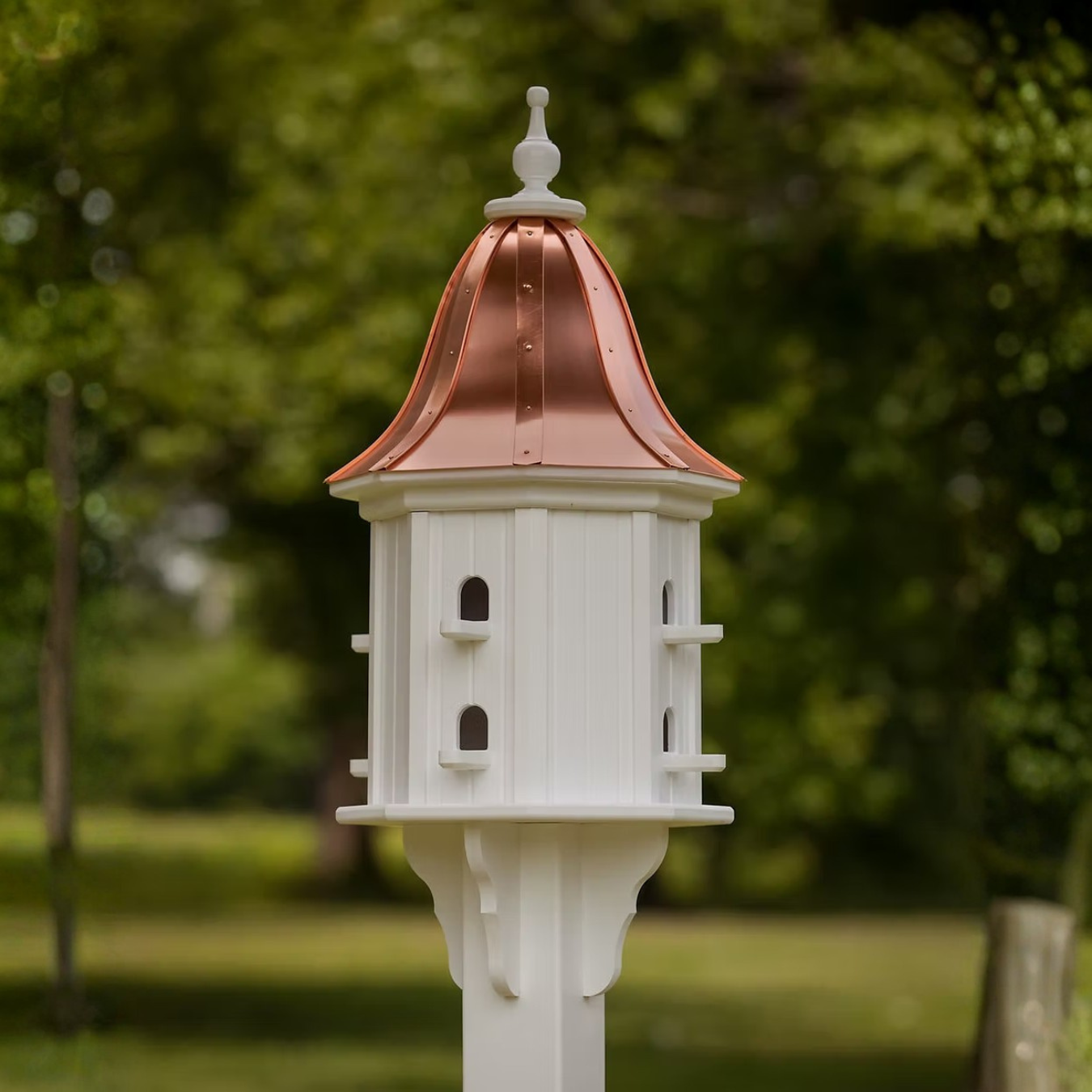 White decorative birdhouse with a bell shaped copper roof in a garden setting