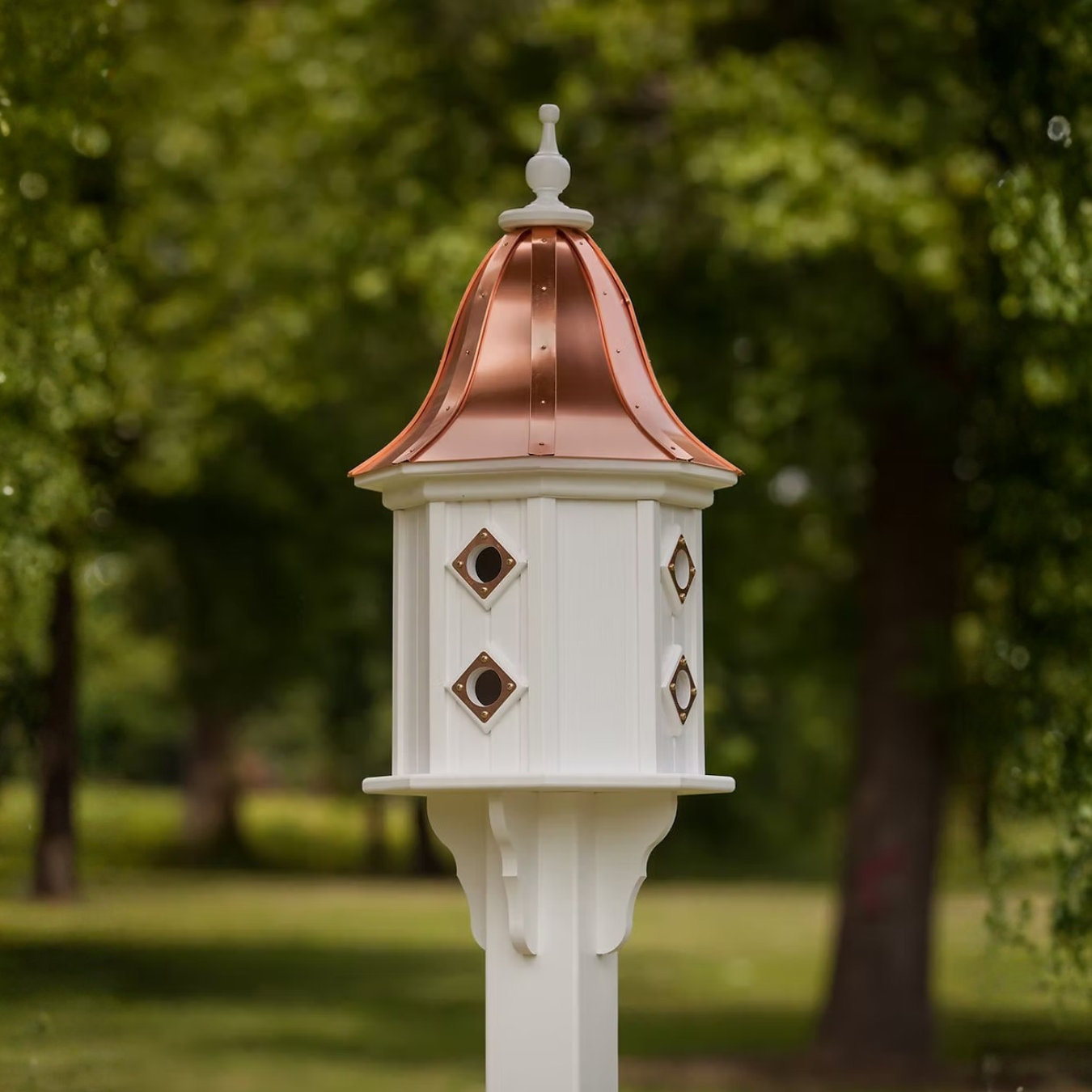 White birdhouse with multiple copper portals and a bell shaped copper roof in a garden setting