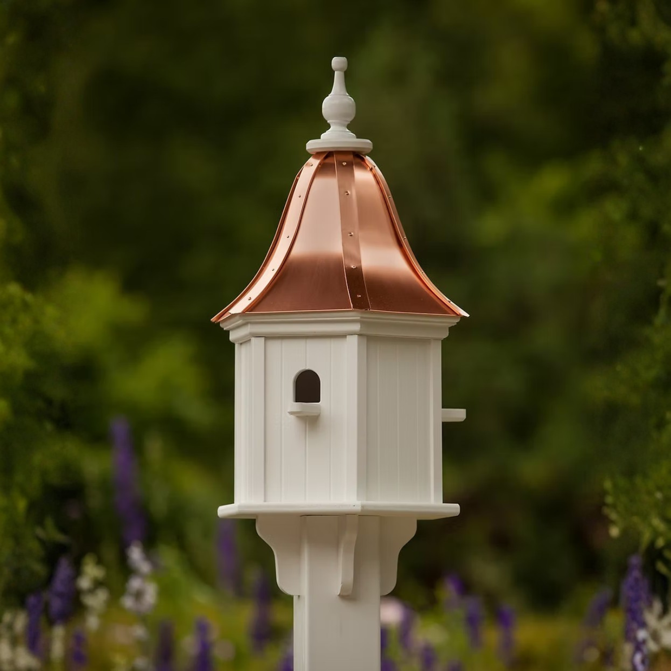 Decorative white birdhouse with bell shaped copper roof in a blurred green garden