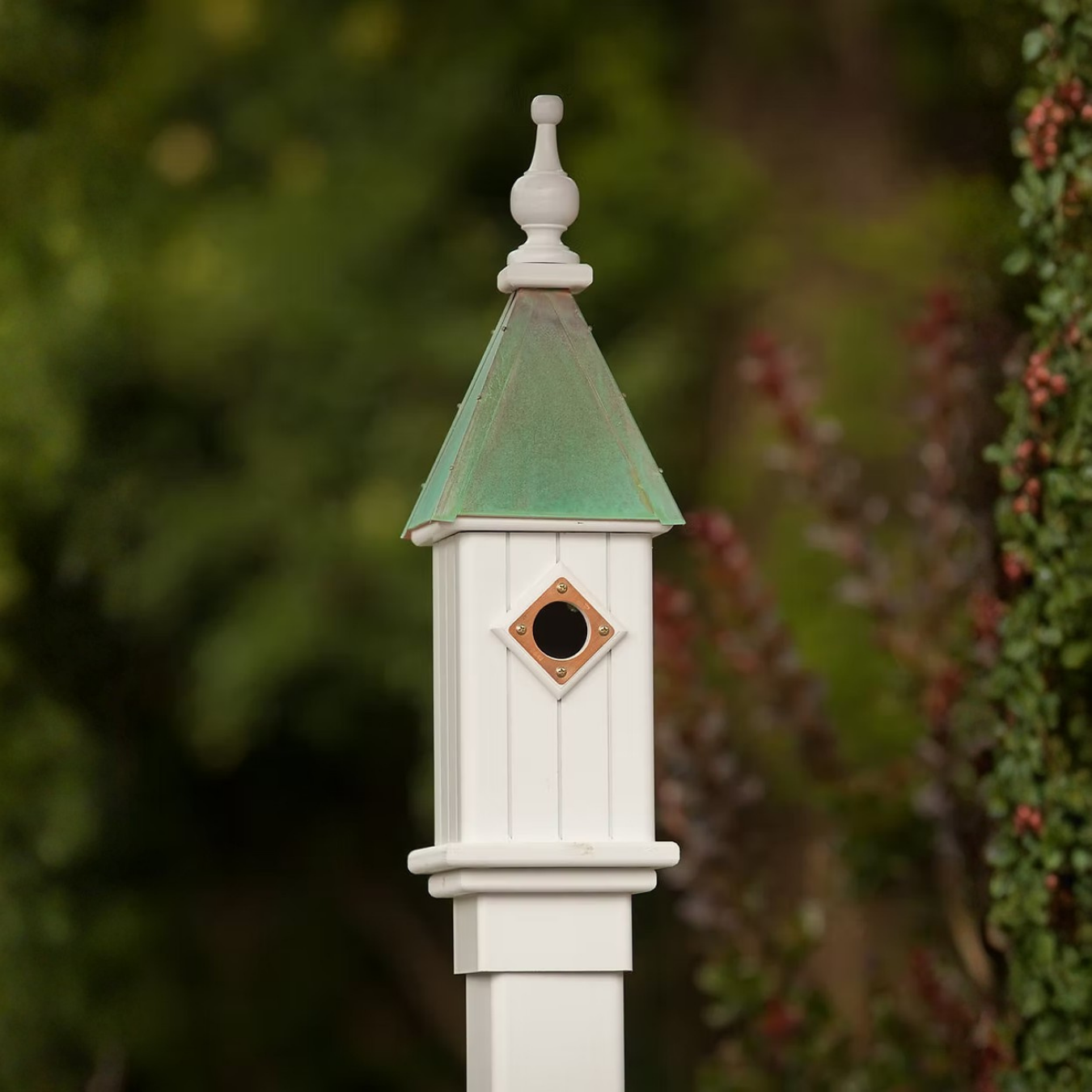 White birdhouse with patina copper roof against a blurred natural background