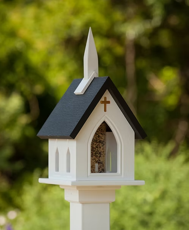 Bird feeder shaped like a church with a cross on a blurred green background