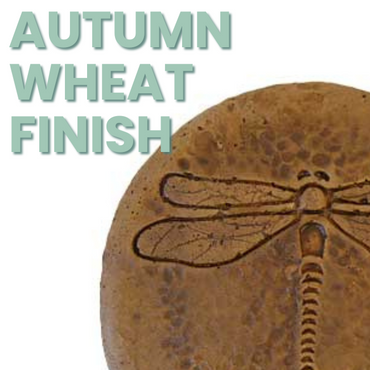 A single handcrafted dragonfly concrete stepping stone on a gravel pathway, with intricate wing impressions and an autumn wheat finish.