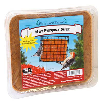 A 3-pound square suet cake labeled "Hot Pepper Suet" from Pine Tree Farms, packaged in a clear plastic container. The label features a bird feeder with orange suet, a woodpecker, and a cardinal. A yellow starburst reads "Birds Love It! Squirrels Don't!" The label includes red, white, and blue branding and a description of the product's spicy formula designed to deter squirrels.