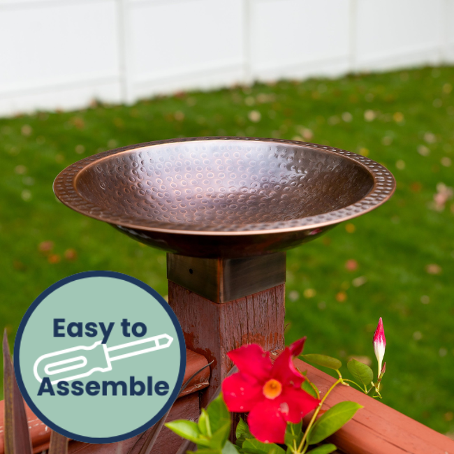 Perch & Ponder Copper Birdbath placed on a wooden post in a garden, with an 'Easy to Assemble' icon highlighting its simplicity.