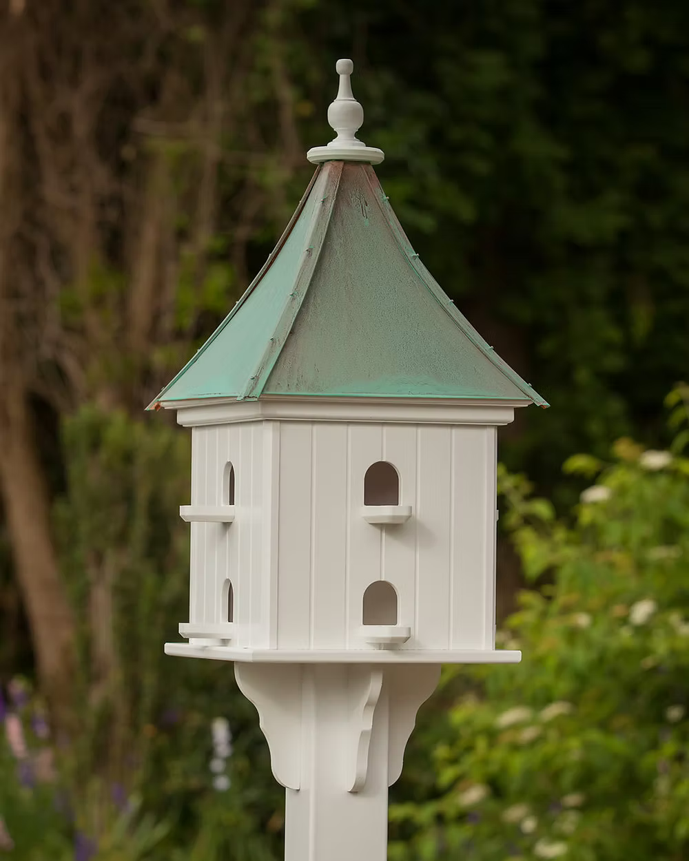 White birdhouse with a patina copper roof in a garden setting