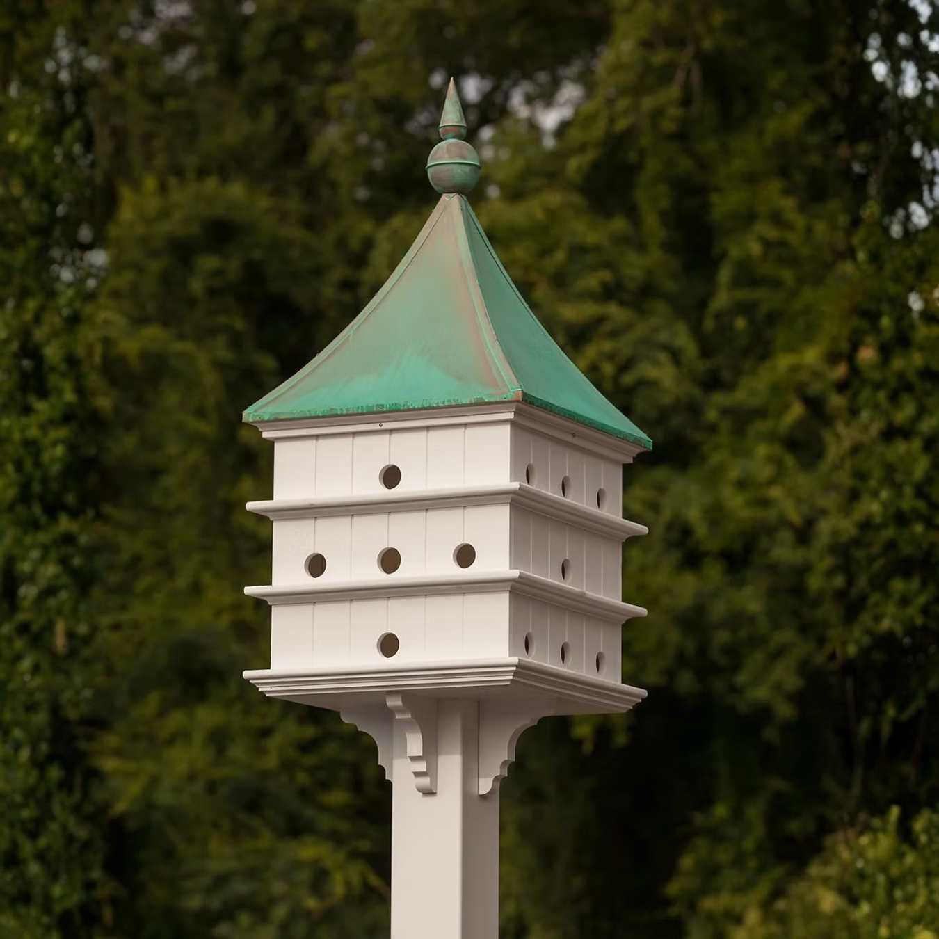 Grand estate Purple Martin white birdhouse with a patina copper roof against a blurred green background