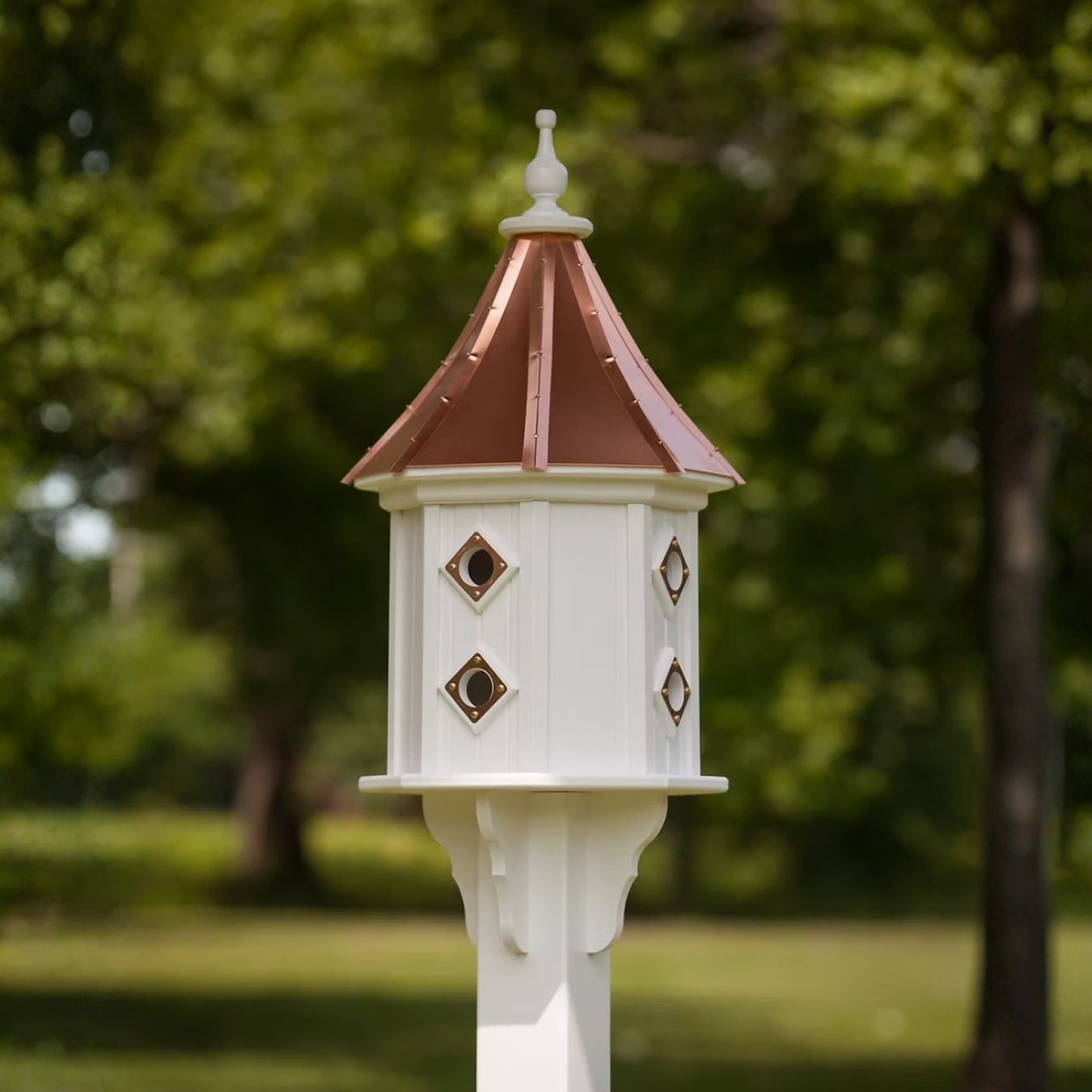 Decorative white birdhouse multiple portal entry's and a slopped copper roof in a garden setting