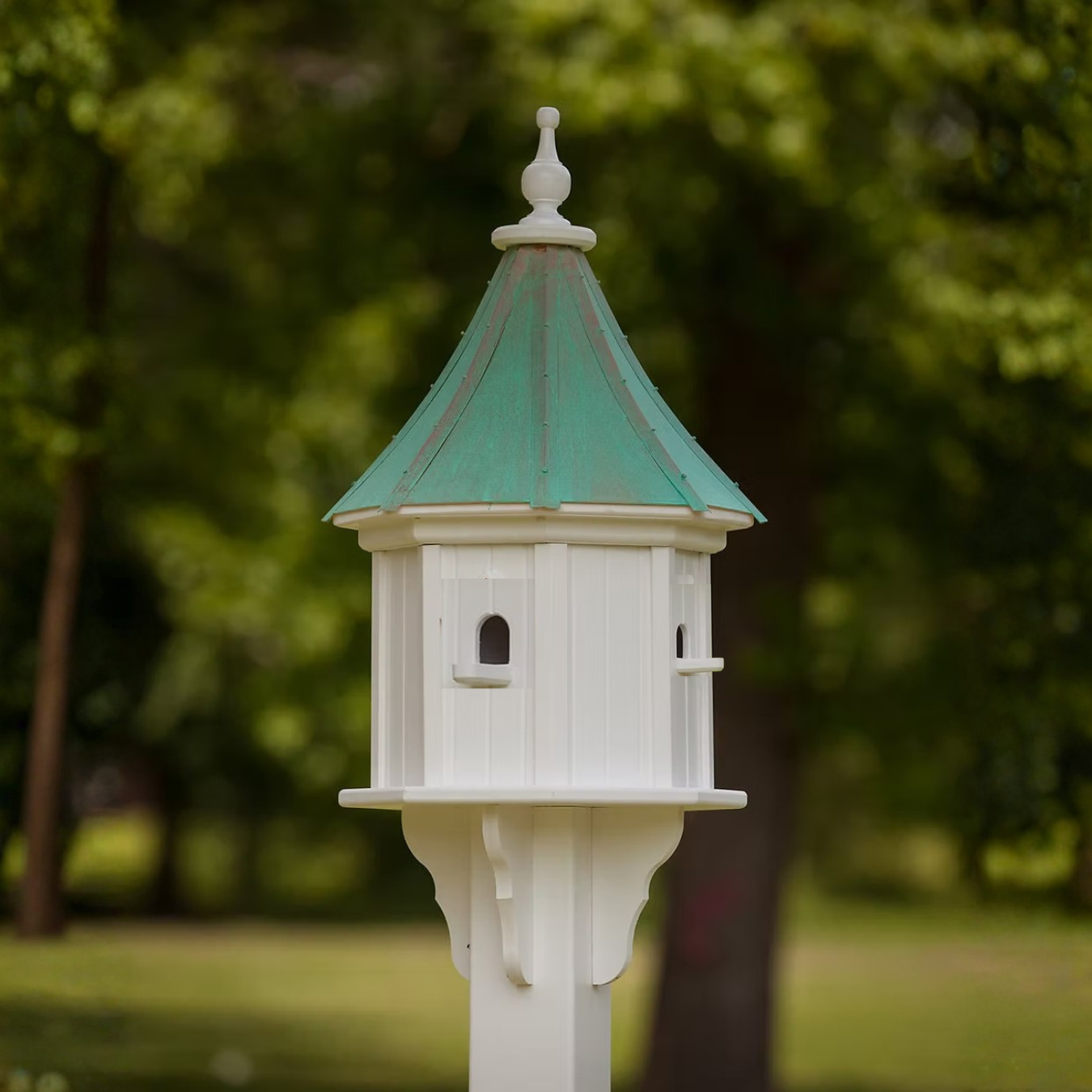 White birdhouse with multi entry perches and a patina copper roof in a garden setting