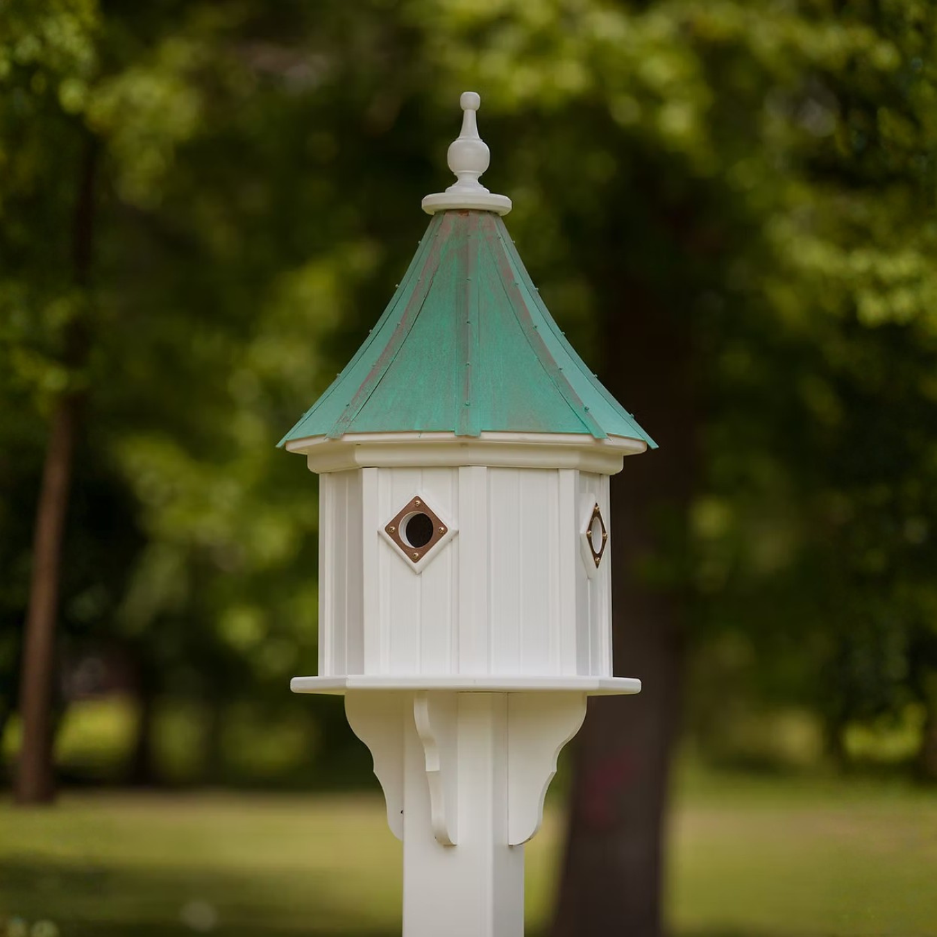 White birdhouse with multiple copper portal entry's and a patina copper roof in a garden setting