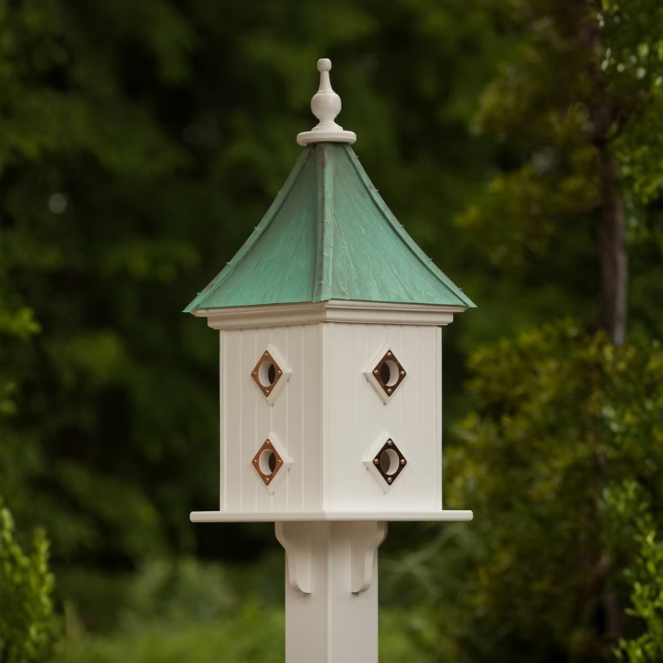 Decorative square birdhouse with multiple copper portal entries and a patina copper roof against a blurred natural background