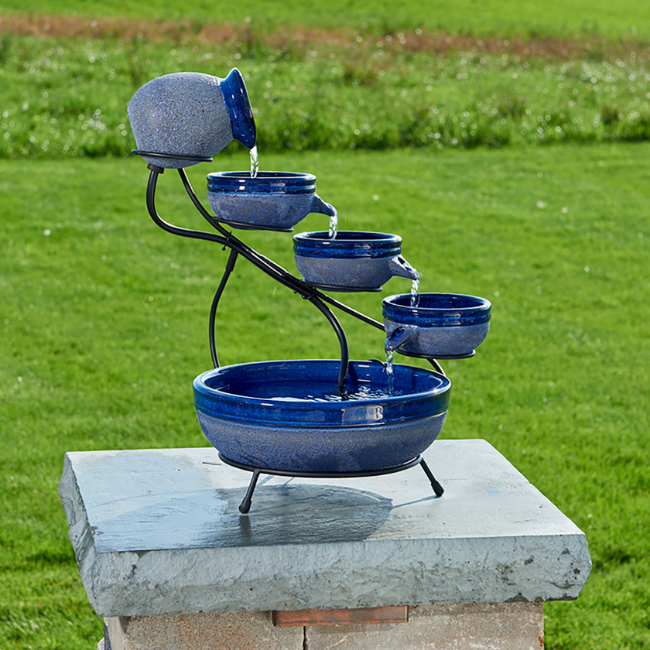 A blue cascading solar fountain with 4 tiers in a grassy area.