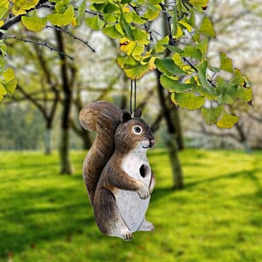 Squirrel-shaped bird feeder hanging from a tree branch with a blurred green garden background