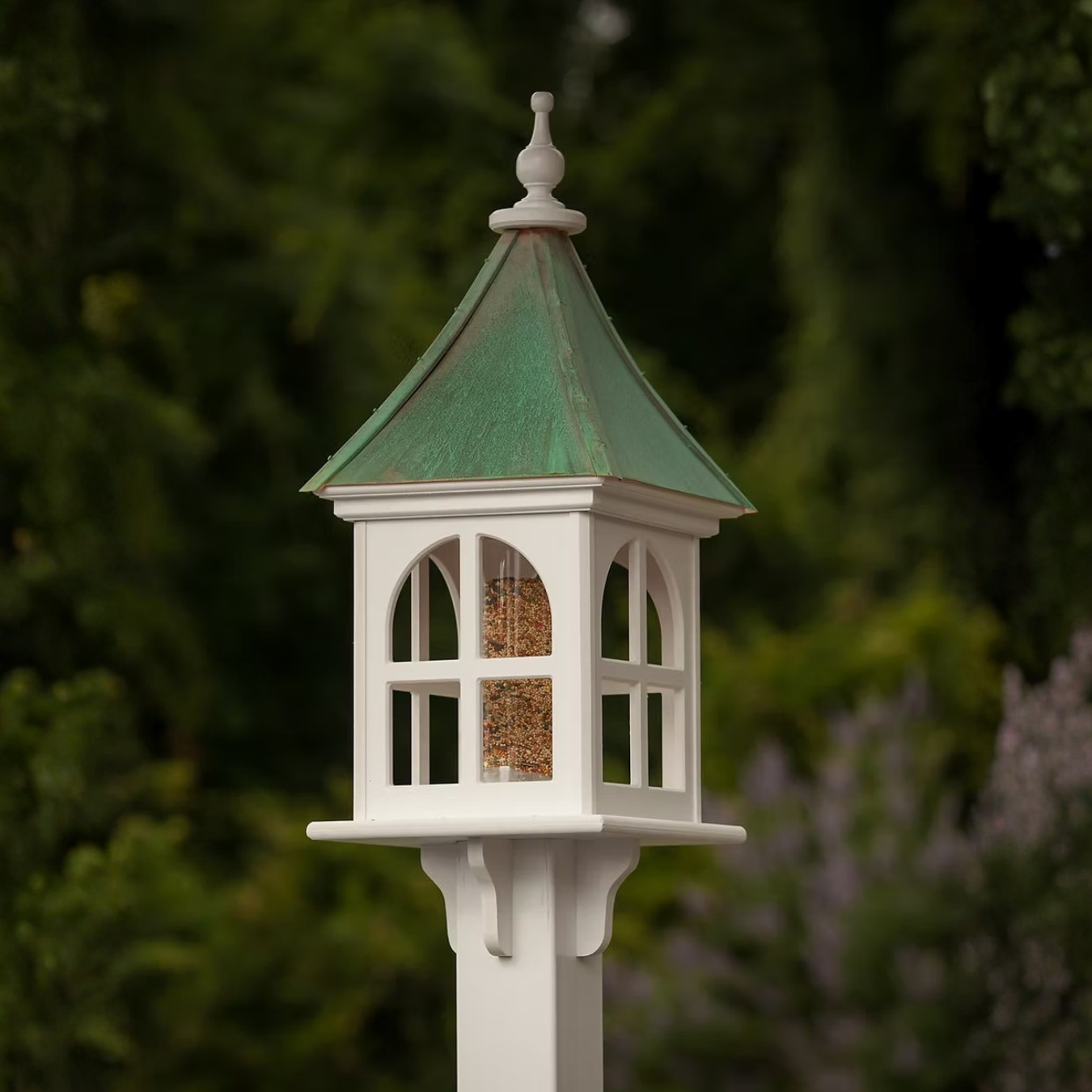 White bird feeder with windows and a patina copper roof against a blurred natural background