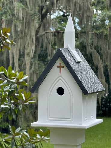 White birdhouse with a black roof and cross on a green background