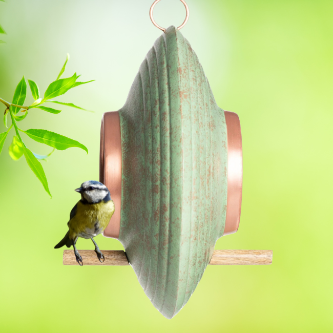 Blue tit bird standing on the side wooden perch of the Fly-Thru™ feeder, with the green background emphasizing the earthy design.