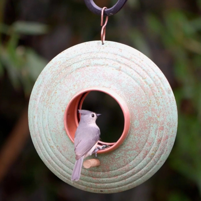 A tufted titmouse bird perched inside the center of the Fly-Thru™ feeder, pecking at seed in the copper-ringed opening.