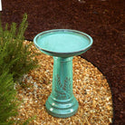 Turquoise ceramic bird bath on a pebble-covered ground with plants in the background