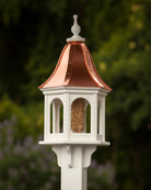 Decorative bird feeder with copper roof against a blurred green background