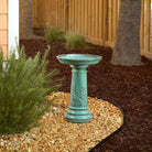 Turquoise bird bath in a garden setting with plants and mulch.