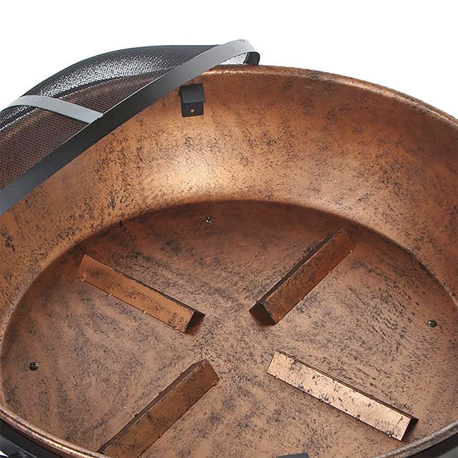 Close-up of a round, copper-toned fire pit interior with a mesh cover partially visible. The texture appears rustic and weathered, conveying warmth.