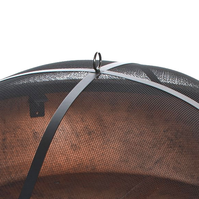 Close-up of a black mesh fire pit cover with a metal handle on top. The mesh curves over, casting shadows underneath, indicating a protective function.