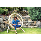 Man sitting in a circular wooden swing chair in a garden setting.