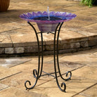 Decorative glass bird bath on a metal stand outdoors.