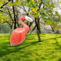 Pink flamingo ornament hanging from a tree branch with green leaves and grass in the background