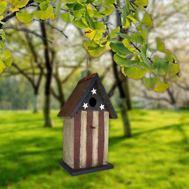 Decorative birdhouse with American flag design hanging from a tree branch.