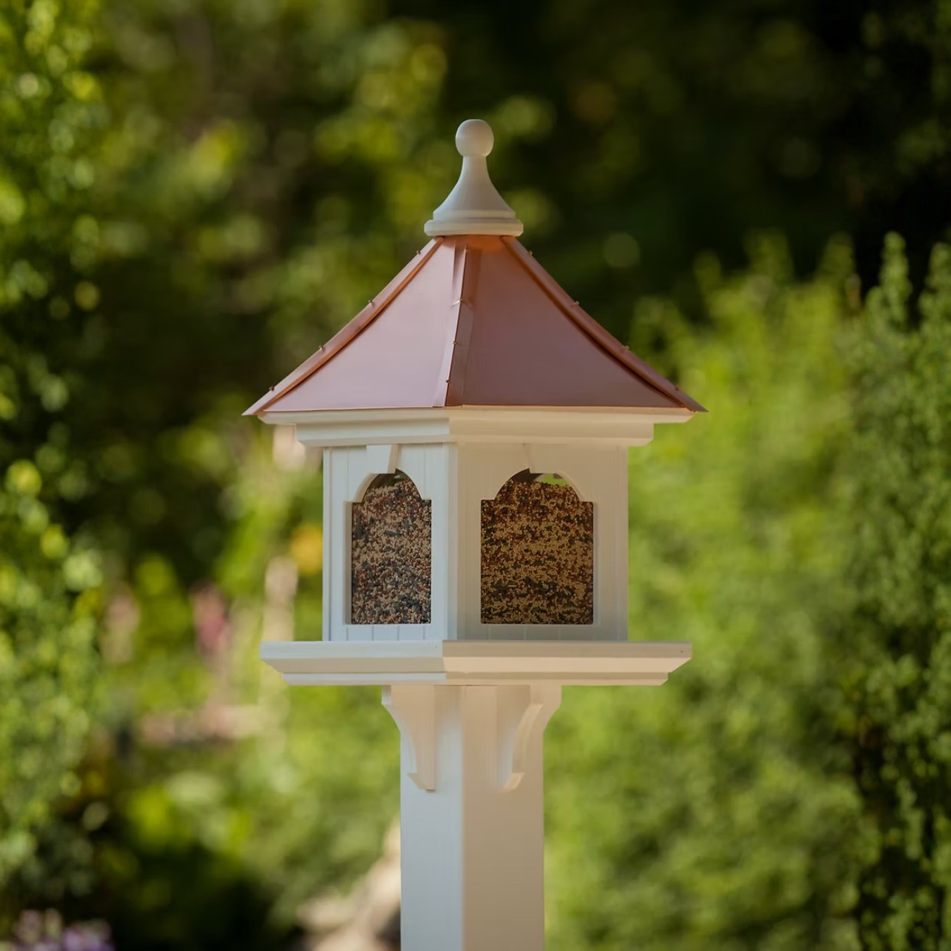 Decorative bird feeder with a white base and Copper roof against a green blurred background