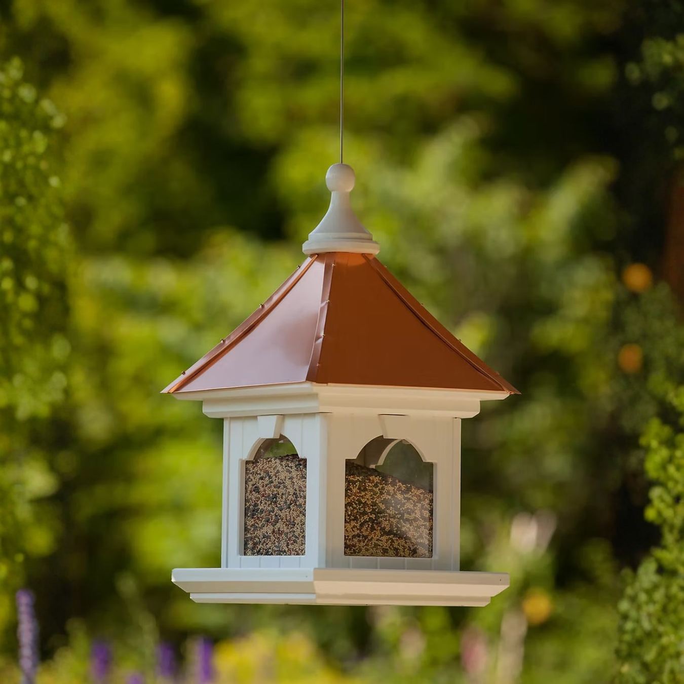 Decorative bird feeder hanging with a copper roof against a green blurred background