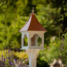 Decorative bird feeder with a copper roof on a stand with a blurred green garden background