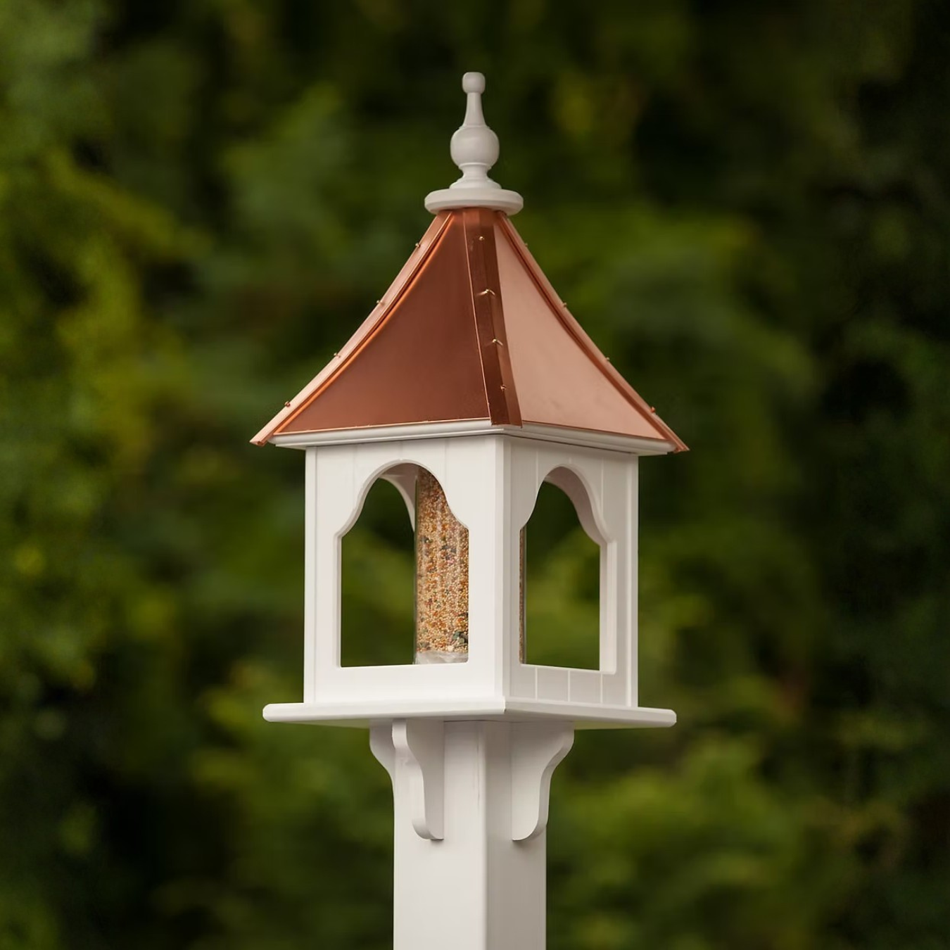 Decorative bird feeder with a copper roof against a blurred green background