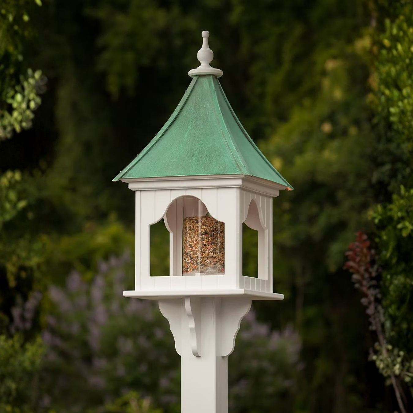 Decorative bird feeder with patina copper roof and white base against a blurred natural background