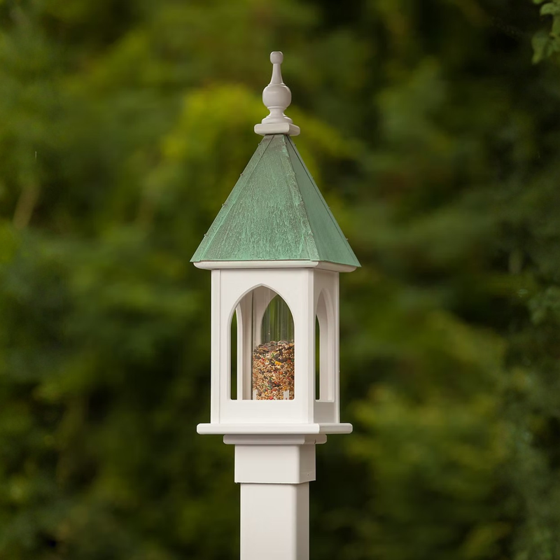 Bird feeder with patina copper roof and white base against a blurred green background