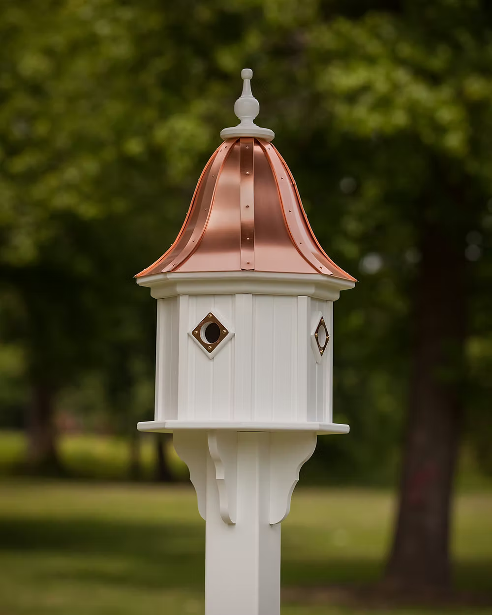 Decorative white birdhouse with a copper roof against a blurred green outdoor background