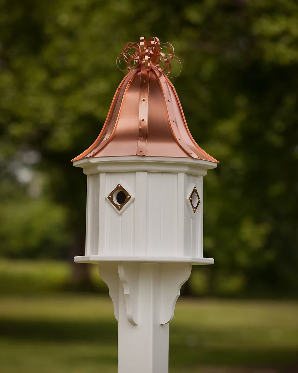 White birdhouse with a copper roof against a blurred green background